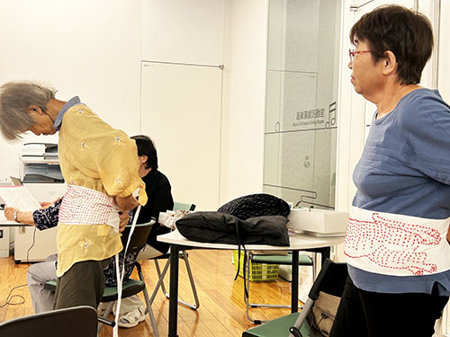 戦争体験を語り継ぐ会　活動のようす　千人針のさらしをおなかに巻くスタッフ