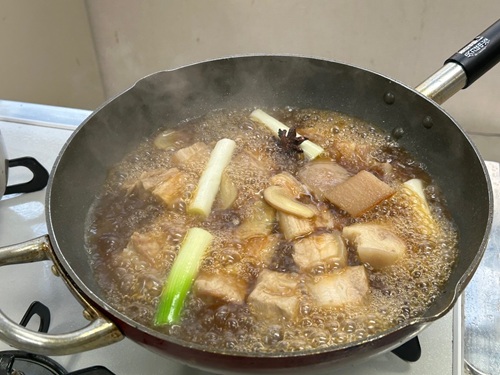 瀬田東国際交流クラブ　活動のようす画像　味付けして、ネギと一緒に煮込まれる豚肉