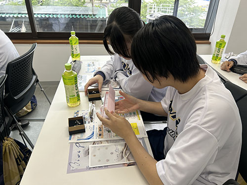 ヴォーリズ倶楽部　北之庄沢・西の湖クリーンプロジェクト　座学の時に見せていただいた、淡水真珠のアクセサリーを見る、女子バスケットボールクラブの生徒たち